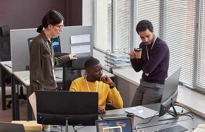 professionals collaborating around a computer, illustrating teamwork and support in Managed IT Services